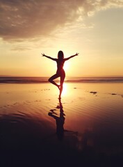 A woman practicing yoga on the beach as the sunsets in