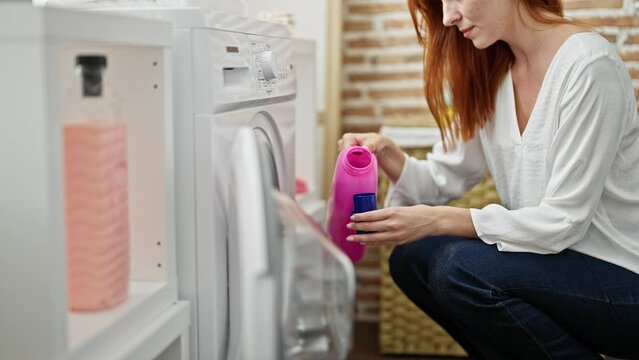 Young redhead woman washing clothes pouring detergent at laundry room