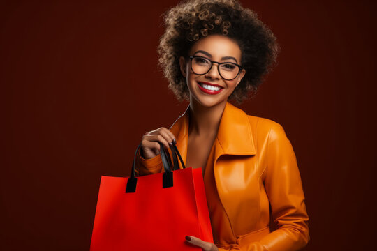 Black girl with afro hair and yellow leather jacket holds a red bag because she has gone black friday shopping.