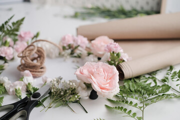 Pink pastel roses and fern leaves on table in flower shop, spring floral background