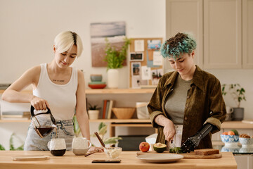Lesbian couple preparing breakfast and making coffee together in the kitchen - obrazy, fototapety, plakaty