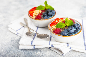 Bowl of granola with yogurt and fresh berries on a texture table. Yogurt berries, acai bowl, spirulina bowl. Healthy food, balanced breakfast. Strawberries, blueberries, kiwi, peach, almonds and chia.