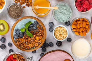 Bowl of granola with yogurt and fresh berries on a texture table. Yogurt berries, acai bowl, spirulina bowl. Healthy food, balanced breakfast. Strawberries, blueberries, kiwi, peach, almonds and chia.