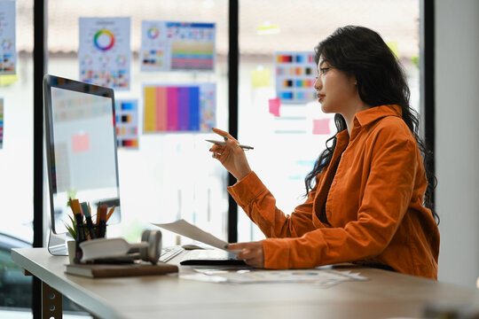 Attractive female freelancer looking at computer monitor, working on new project in creative workplace