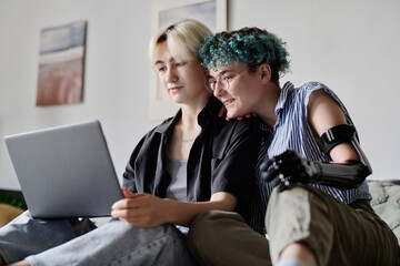 Girlfriends sitting on bed and using laptop together at home