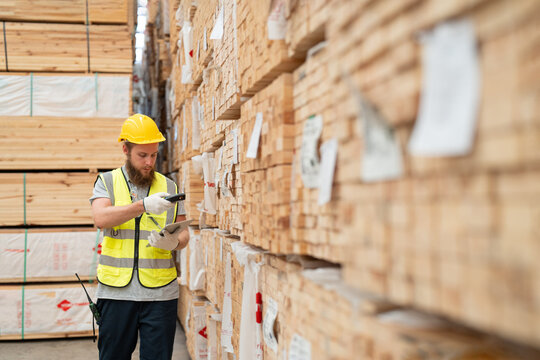 Male worker using scanner machine scanning barcode on label for checking plank wood stock inventory at wooden warehouse. Man worker in uniform and helmet safety working in wood factory.