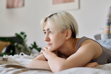 Young woman with short blond hair relaxing on her bed during her free time at home