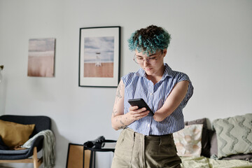 Young woman reading message on her smartphone while standing in the living room