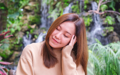 Portrait image of a young woman with closed eyes sitting and relaxing in the garden