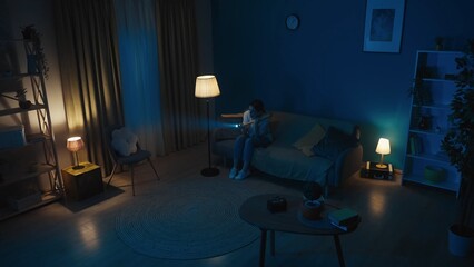 Shot of a young woman sitting on a couch in a dark room, looking around for burglars, intruders, thieves. She holds a baseball bat and a flashlight.