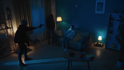 Shot of two burglars standing in front of the couch where the owner of the house, flat sits,...