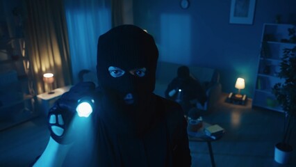 Shot capturing two burglars robbing the apartmnet. One of them stands on the foreground, pointing...