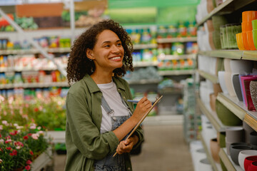 Woman garden shop worker records the quantity of empty pots on shelf while working in flower store