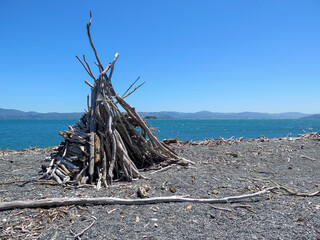 Large man made triangular driftwood structure on a pebble beach in Wellington, New Zealand.