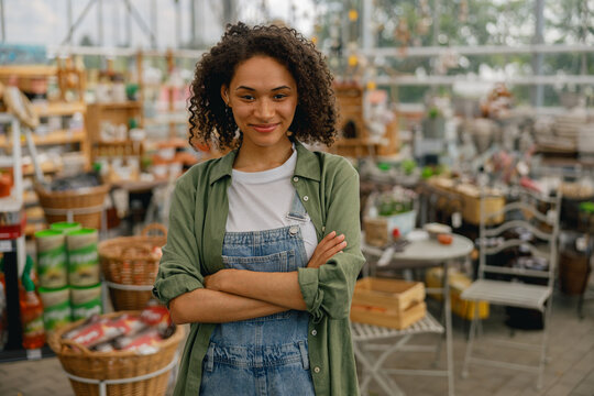 Smiling female garden shop seller standing on flower store background. Gardening concept