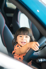Portrait photo of a cute baby girl is joying to sitting and control the steering wheel on car driver seat.