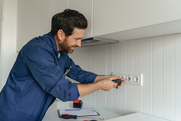 Professional electrician using screwdriver while installing new electrical socket on home kitchen