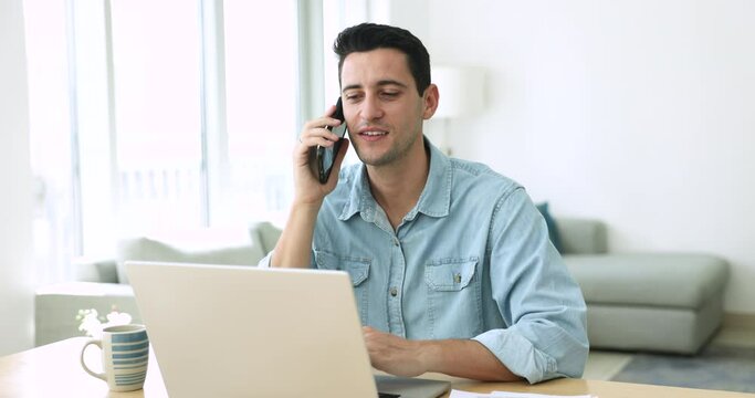 Handsome positive Hispanic businessman talk to client on cellphone seated at desk with laptop, get or give consultation remotely by phone call, contact to customer services, making order via website