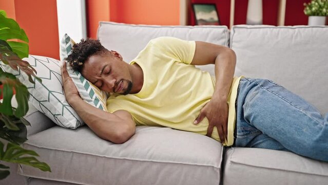 African american man suffering for stomach ache lying on sofa at home