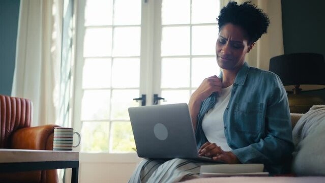 Menopausal mature woman at home with laptop having hot flush and fanning herself with letter - shot in slow motion
