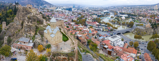 Panoramic drone view of Old Town, Narikala Fortress, Saint Nicholas's Church and Kura river on cloudy autumn day. Tbilisi, Georgia. - obrazy, fototapety, plakaty