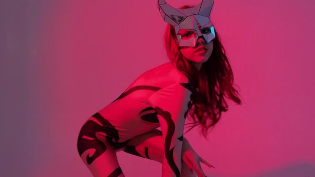A devil girl with horns on her head in a sexy tight costume dances beautifully in the studio in red neon light.