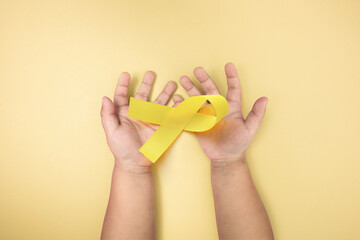 child cancer awareness, a yellow ribbon in children hands on yellow background, world cancer day, february 4, healthcare and medicine backdrop, suicide prevention, children health care.