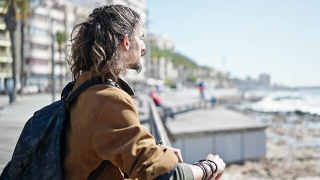 Young hispanic man tourist wearing backpack leaning on balustrade at seaside