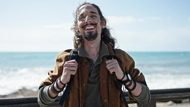Young hispanic man tourist wearing backpack smiling at seaside