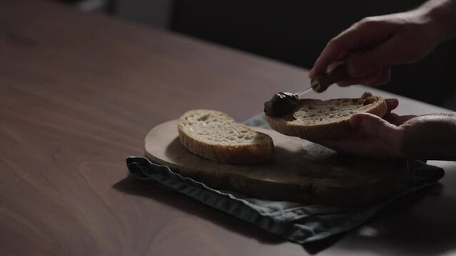 Slow motion man spreading chocolate spread on ciabatta slice on olive board