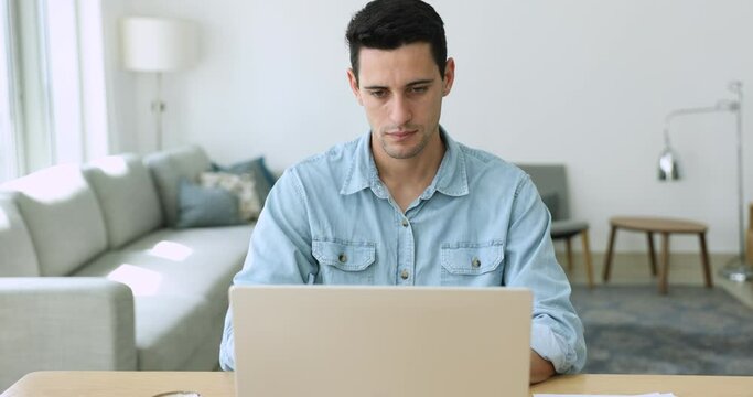 Serious Hispanic business man sit at desk use laptop feels stressed and angry due to awful online news in e-mail, computer malware, unsaved document, lost important information. Broken device, problem