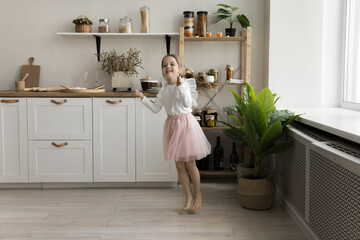 Cheerful little ballet dancer girl in pink princess skirt dancing to music at home, jumping, flying in air, enjoying active game, leisure, motion alone, exercising for choreography class