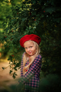 Portrait of a blonde little girl in a red beret and a plaid dress