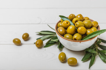 Greens olives on a white wooden background. Various types of olives in bowls and olive oil with...
