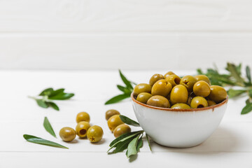 Greens olives on a white wooden background. Various types of olives in bowls and olive oil with fresh olive leaves. Copy space. Place for text. Mediterranean food. Vegan.