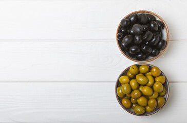 Green and black olives on a white wooden background. Various types of olives in bowls and olive oil with fresh olive leaves. Copy space. Place for text. Mediterranean food. Vegan.