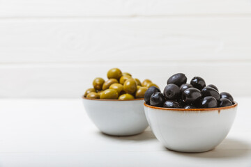 Green and black olives on a white wooden background. Various types of olives in bowls and olive oil with fresh olive leaves. Copy space. Place for text. Mediterranean food. Vegan.