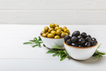 Green and black olives on a white wooden background. Various types of olives in bowls and olive oil with fresh olive leaves. Copy space. Place for text. Mediterranean food. Vegan.