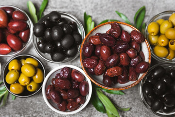 A set of green, red and black olives on a marble background. Various types of olives in bowls and fresh olive leaves. Vegan. Olive fruits. Place for text. Copy space.