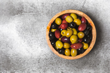 A set of green, red and black olives on a marble background. Various types of olives in bowls and fresh olive leaves. Vegan. Olive fruits. Place for text. Copy space.