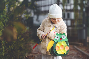 Little preschool kid girl holding selfmade traditional owl lanterns with candle for St. Martin...