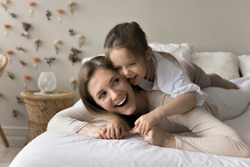 Happy laughing mom playing active games with toddler child at home, piggybacking adorable kid on double bed, enjoying funny family activities, childcare, motherhood