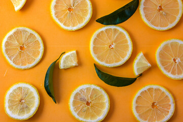 Obraz premium Lemon slices adorned with green leaves on an orange background offer a vivid and tropical display