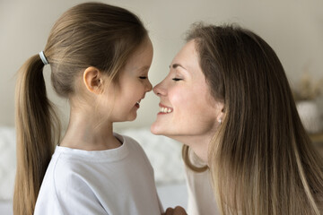 Cheerful loving mom kissing pretty little daughter kid with faces, noses touch, closed eyes, cuddling child with affection, care, tenderness, enjoying motherhood, family moment