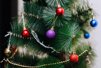 Beautiful colored Christmas, New Year's toys, balls, garland, decorations hang on a branch of a decorated spruce, a green tree. Close-up photography, holiday, background.