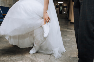 The bride in a white dress puts on, straightens sports sneakers on her feet. Wedding photography,...