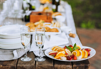 A round fruit plate, champagne glasses stand on a wooden table at a banquet. Photo of food, dessert, buffet at the holiday.