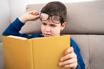 Child suffering eye strain trying to read a book at home - obrazy, fototapety, plakaty