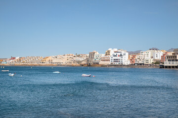 Fototapeta na wymiar View from across the pier of the little picturesque town, perfect summer vacation destination for tourists interested in doing watersports, El Medano, Tenerife, Canary Islands, Spain