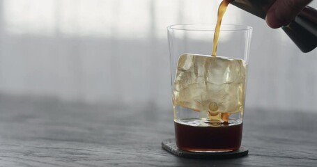 Slow motion coffee pour over ice cube in tumbler glass on black wood table - Powered by Adobe